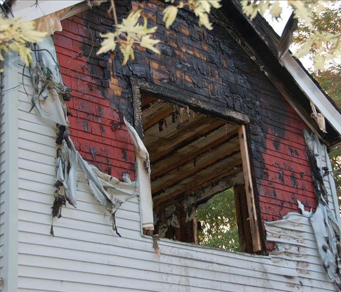 Fire damaged home with melted siding and broken glass