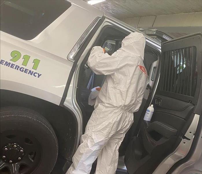 hazmat suit wearing man disinfecting 911 emergency vehicle